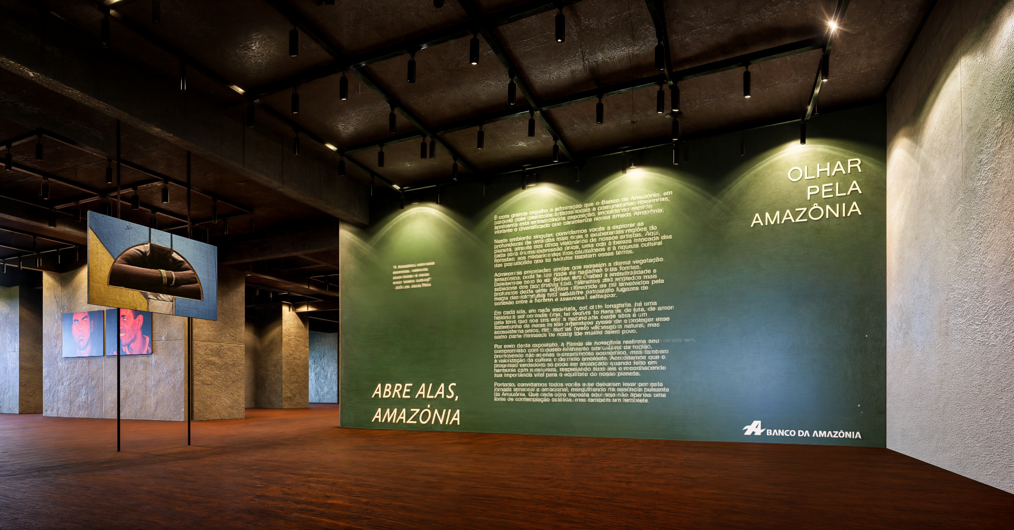 Galeria expositiva com parede verde e iluminação em trilho